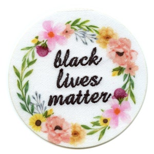 May include: White circular patch with a floral wreath surrounding the text "black lives matter" in black embroidery.