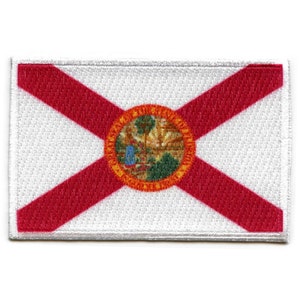 May include: A white patch with a red diagonal cross and a seal in the centre. The seal is a circle with a yellow outer ring, a green inner circle, and a white palm tree in the centre. The seal has the words "Great Seal of the State of Florida" around the outer edge.