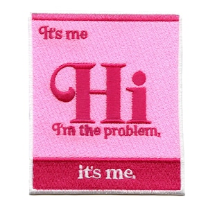 May include: A pink embroidered patch with the words "It's me" at the top and bottom. The word "Hi" is in large, bold, pink letters in the center, with the phrase "I'm the problem" below it.