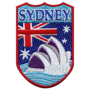 May include: Embroidered patch with a blue background, a red, white, and blue Australian flag, and a white outline of the Sydney Opera House. The text "SYDNEY" is in blue letters at the top of the patch.