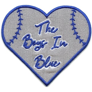 Può includere: Una toppa a forma di cuore con sfondo grigio e cuciture blu sui bordi. Il testo "The Boys In Blue" è ricamato in blu con un carattere corsivo. La toppa è progettata per assomigliare a una palla da baseball.