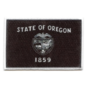 May include: A black and white embroidered patch featuring the text "STATE OF OREGON" and the state seal, which depicts a wagon and a mountain range, with the year "1859" below the seal.
