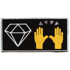 May include: Black embroidered patch with a white diamond and two yellow hands raised in the air with three gray stars above them.