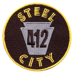 Puede incluir: Un parche bordado marrón y amarillo con el texto "STEEL CITY 412" en una fuente estilizada. El número 412 está dentro de un contorno gris del estado de Pensilvania.