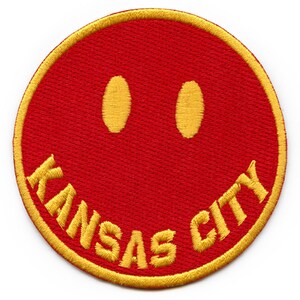 May include: A red embroidered patch with a yellow smiley face and the text "KANSAS CITY" around the edge.
