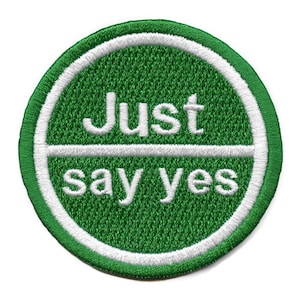 Könnte beinhalten: Ein grüner und weißer gestickter Aufnäher mit dem Text "Just say yes" in einem Kreis.