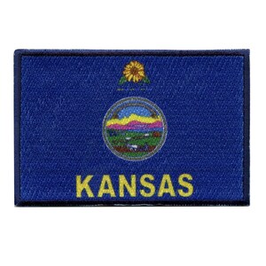 May include: A blue embroidered patch with the state seal of Kansas. The seal features a sunflower, a river, and a sun. The word "KANSAS" is written in yellow letters below the seal.