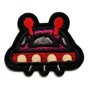 May include: A black felt embroidered patch of a cartoon spaceship with red and white details. The spaceship has a rounded top with two red antennas and a bottom with three white circles.