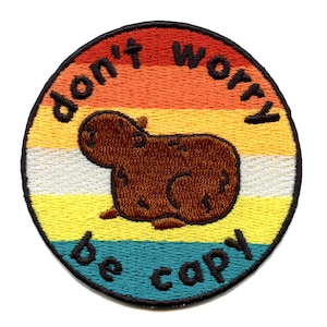 Op de afbeelding: Een ronde geborduurde patch met een regenboogachtergrond. De patch heeft een cartoon capybara en de tekst "don't worry be capy".