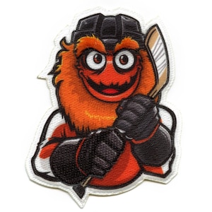 Puede incluir: Una mascota de hockey naranja y negra con un sombrero negro y un palo de hockey. La mascota tiene una gran sonrisa y lleva una camiseta de hockey.
