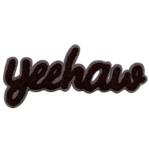 May include: A dark brown felt patch with the word "yeehaw" in a cursive font. The lettering has a gray outline, and the patch is on a white background. This patch is suitable for clothing or accessories.