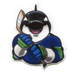 May include: A blue and green hockey patch featuring a cartoon orca wearing a hockey jersey and holding a hockey stick. The orca has a white face and black eyes.