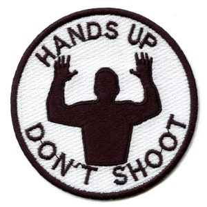 May include: White circular patch with black embroidered text that reads "Hands Up Don't Shoot" and a black silhouette of a person with their hands raised in the air.