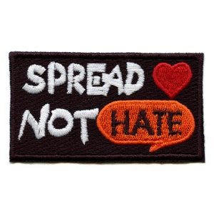 Op de afbeelding: Een rechthoekige patch met de woorden "SPREAD NOT HATE" in wit geborduurd op een donkerbruine achtergrond. Een rood hart en een oranje tekstballon met het woord "HATE" zijn ook afgebeeld.