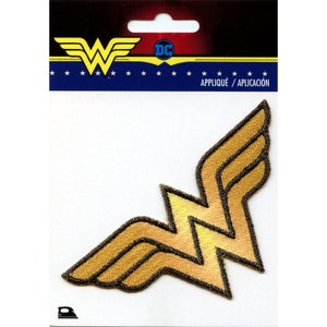 May include: Gold Wonder Woman logo iron-on patch with a black outline. The patch is packaged on a white card with a blue header that says "DC" and "Appliqué/Aplicación".