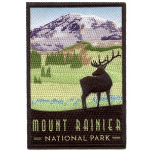 May include: Embroidered patch featuring Mount Rainier National Park. The patch depicts a mountain range, a deer, and the text "Mount Rainier National Park" in a rectangular frame. The patch has a brown border and a blue, green, and brown colour scheme.