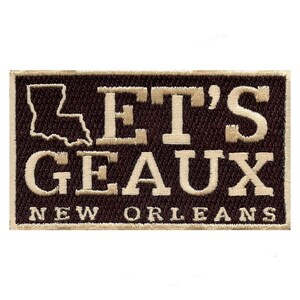 Op de afbeelding: Een bruin geborduurd patch met de tekst "Let's Geaux New Orleans" en een omtrek van de staat Louisiana.