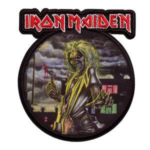 May include: Iron Maiden band patch featuring a black and yellow illustration of Eddie, the band's mascot, holding a bloody knife. The patch is circular and has a black border with white stitching. The band's name is written in red and white letters above the illustration.