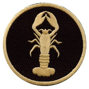 Op de afbeelding: Een gouden geborduurde patch met een zwarte achtergrond met een kreeftontwerp.