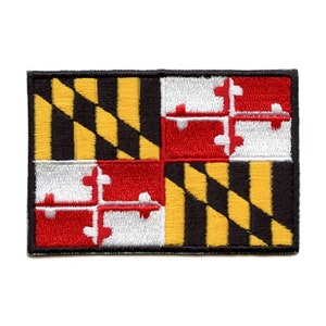 May include: An embroidered patch featuring the Maryland state flag. The flag is a black and gold checkered pattern with a red and white quartered design in the center.