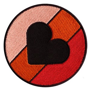 Könnte beinhalten: Ein runder gestickter Aufnäher mit einem schwarzen Herzen in der Mitte. Das Herz ist teilweise von drei Stoffstreifen in den Farben Rosa, Orange und Rot bedeckt.