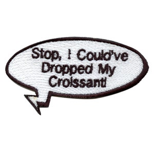 May include: White oval-shaped embroidered patch with a brown outline and a speech bubble design. The text inside the speech bubble reads "Stop, I could've dropped my croissant."