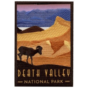 Op de afbeelding: Een geborduurde patch met een bruin silhouet van een dikhoornschaap tegen een achtergrond van een woestijnlandschap met een paarse en blauwe lucht. De tekst "DEATH VALLEY NATIONAL PARK" is geborduurd in goud op een zwarte achtergrond.