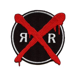 Può includere: Una toppa ricamata in bianco e nero con una X rossa sulle lettere "RR" in bianco. La X cola di vernice rossa.