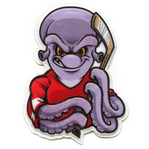 Op de afbeelding: Paarse octopus cartoonfiguur met een rood-wit hockeytrui aan en een hockeystick vasthoudend. De octopus heeft een dreigende uitdrukking met een brede, tandenrijke grijns.