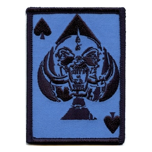 Könnte beinhalten: Ein blauer gestickter Aufnäher mit einem schwarzen Pik-Ass. Das Pik-Ass zeigt einen Schädel mit einem bedrohlichen Ausdruck.