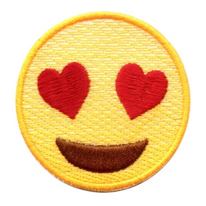 May include: Embroidered patch featuring a yellow emoji face with red heart-shaped eyes and a brown smile. The patch has a yellow border and is designed to be ironed or sewn onto fabric. Ideal for clothing or accessories.
