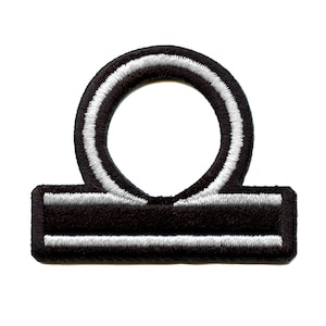 May include: Black and white embroidered iron-on patch of the astrological symbol for Libra.