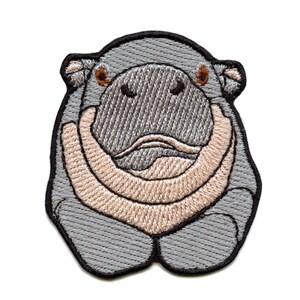 May include: Embroidered patch featuring a gray hippo with a light tan snout and a black outline. The hippo's face is detailed with brown eyes and a textured appearance. This patch is suitable for clothing or accessories.