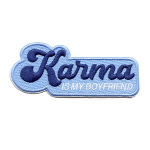 May include: A light blue embroidered patch with the word "Karma" in dark blue script. Below, the text "IS MY BOYFRIEND" is in white. The patch has a white border and a unique shape.