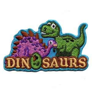 Puede incluir: Un parche bordado con dos dinosaurios de dibujos animados, uno verde y otro morado, con la palabra "DINOSAURIOS" en letras marrones sobre un fondo azul.