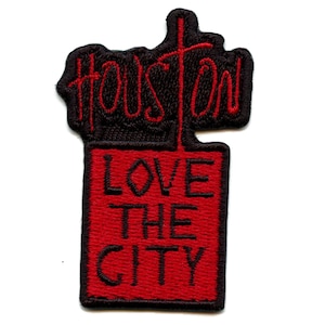 Può includere: Toppa ricamata con la scritta "Houston" in rosso sopra un rettangolo rosso con le parole "LOVE THE CITY" in nero. La toppa ha un bordo nero.