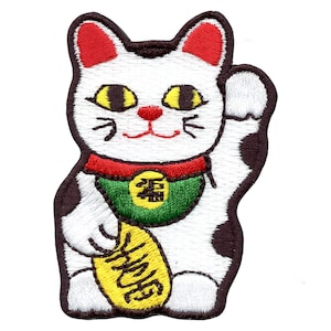 May include: White and brown embroidered lucky cat with red ears and a green collar. The cat is holding a gold coin with Japanese characters.