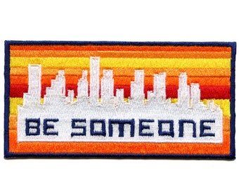 May include: White embroidered patch featuring a cityscape silhouette and the text "BE SOMEONE" in a retro style. The background is a gradient of orange, yellow, and red.