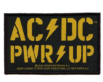 Op de afbeelding: Een zwart en geel geborduurd patch met de tekst "AC/DC PWR UP" en het AC/DC-bliksemlogo. De tekst "2020 LEIDSEPLEIN PRESSE B.V. UNDER LICENSE TO PERRYSCOPE PRODUCTIONS, LLC/EPIC RIGHTS, LLC" is onder het logo gedrukt.