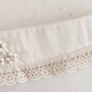 Puede incluir: Un cuello de tela blanca con ribete de encaje y adornos de perlas.