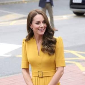 Pu&ograve; includere: Una donna con un vestito giallo con scollo a V e cintura. Ha i capelli lunghi e castani e sorride.