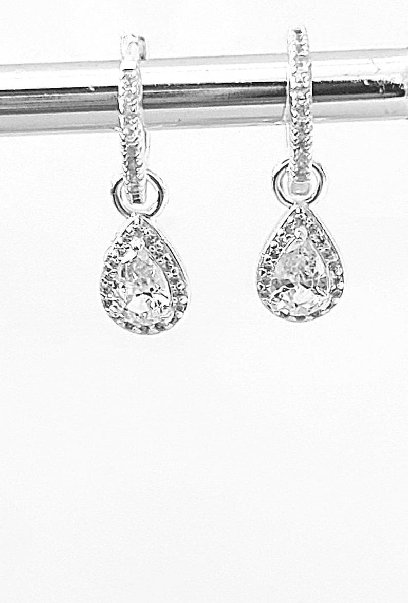 Pu&ograve; includere: Un paio di orecchini a cerchio d'argento con ciondoli a goccia di cristallo trasparente a forma di pera.