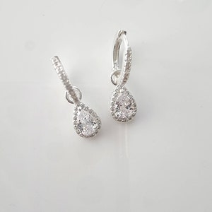 Pu&ograve; includere: Un paio di orecchini a cerchio d'argento con un ciondolo di cristallo a forma di lacrima. Il cristallo &egrave; circondato da un'aureola di cristalli pi&ugrave; piccoli.