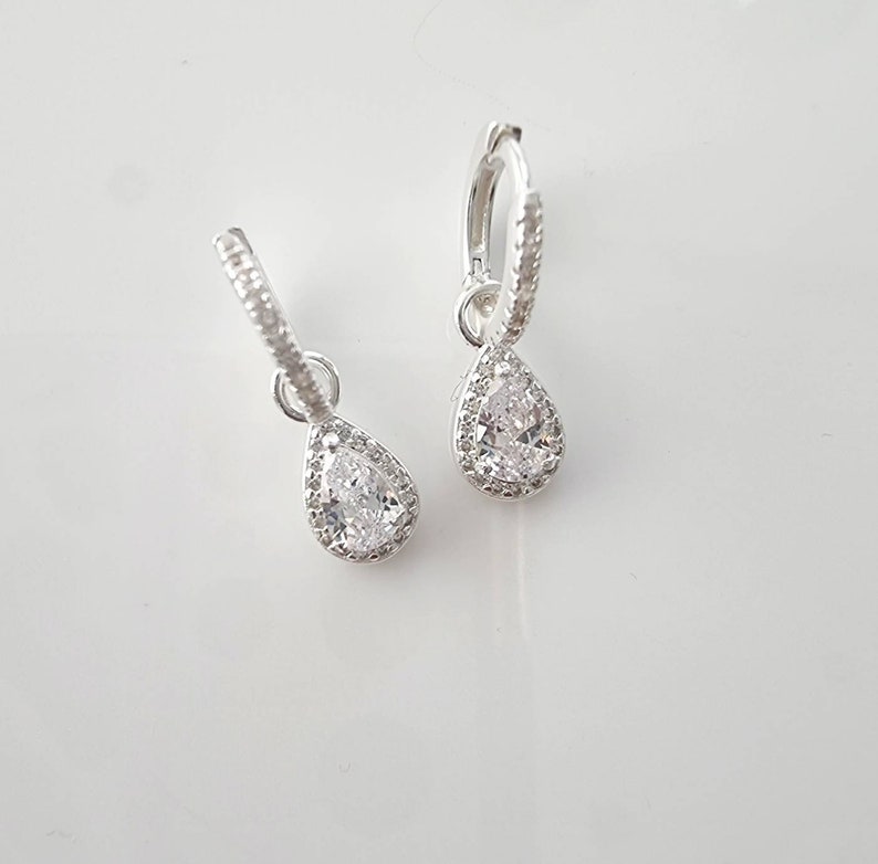 Pu&ograve; includere: Un paio di orecchini a cerchio d'argento con un ciondolo di cristallo a forma di lacrima. Il cristallo &egrave; circondato da un'aureola di cristalli pi&ugrave; piccoli.