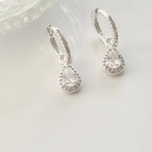 Pu&ograve; includere: Un paio di orecchini a cerchio d'argento con un ciondolo di cristallo a forma di lacrima. Il cristallo &egrave; circondato da un'aureola di cristalli pi&ugrave; piccoli.