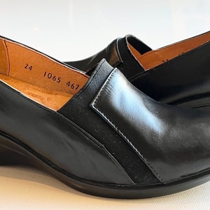 Peut inclure: Une paire de chaussures &agrave; talon compens&eacute; en cuir noir avec un panneau en daim noir sur le c&ocirc;t&eacute;. Les chaussures portent une &eacute;tiquette de taille 24, 1065, 467 &agrave; l'int&eacute;rieur.