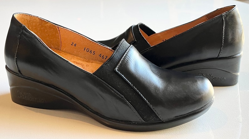 Peut inclure: Une paire de chaussures &agrave; talon compens&eacute; en cuir noir avec un panneau en daim noir sur le c&ocirc;t&eacute;. Les chaussures portent une &eacute;tiquette de taille 24, 1065, 467 &agrave; l'int&eacute;rieur.