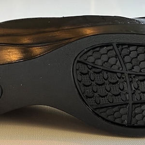 Peut inclure: Chaussure en cuir noir avec une semelle textur&eacute;e. La semelle pr&eacute;sente un motif de petits carr&eacute;s et un motif plus grand de lignes. La chaussure a un petit logo sur le c&ocirc;t&eacute; qui dit "Dr. Scholl's".