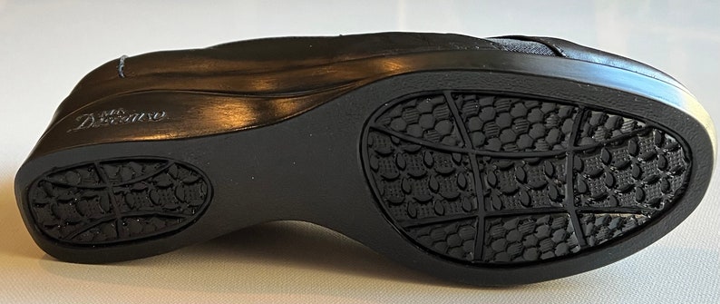 Peut inclure: Chaussure en cuir noir avec une semelle textur&eacute;e. La semelle pr&eacute;sente un motif de petits carr&eacute;s et un motif plus grand de lignes. La chaussure a un petit logo sur le c&ocirc;t&eacute; qui dit "Dr. Scholl's".