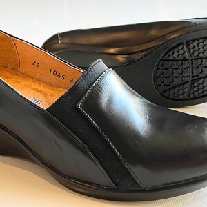 Peut inclure: Chaussures compens&eacute;es en cuir noir avec un panneau en daim noir sur le c&ocirc;t&eacute;. Les chaussures ont une semelle en caoutchouc avec un motif textur&eacute;. La taille 24 est imprim&eacute;e &agrave; l'int&eacute;rieur de la chaussure.